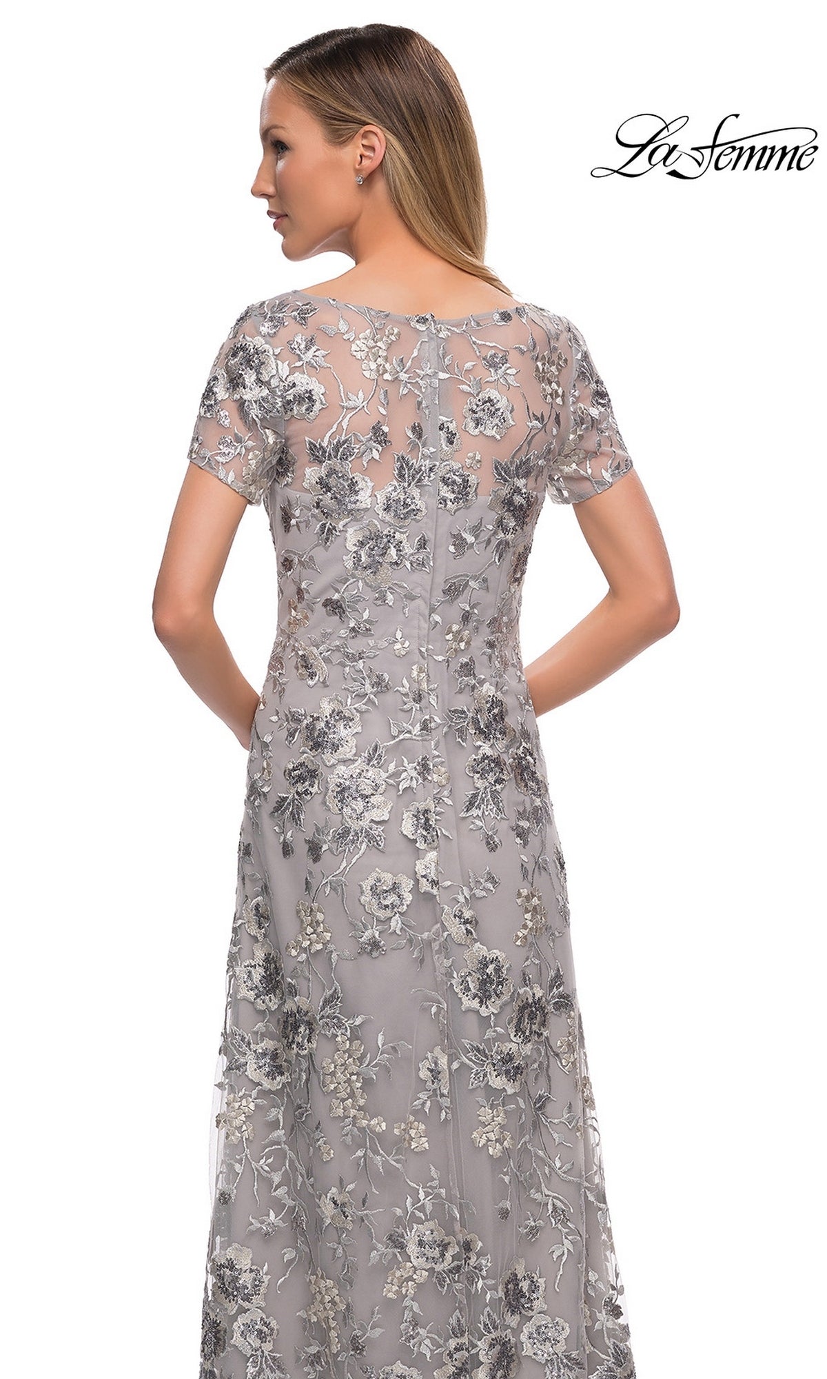 Back view of a woman wearing a modest long silver La Femme 29281 formal dress with short sleeves and floral embroidery.